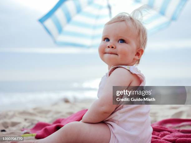 happy little blondhaired toddler girl sitting at the beach. - baby girls foto e immagini stock