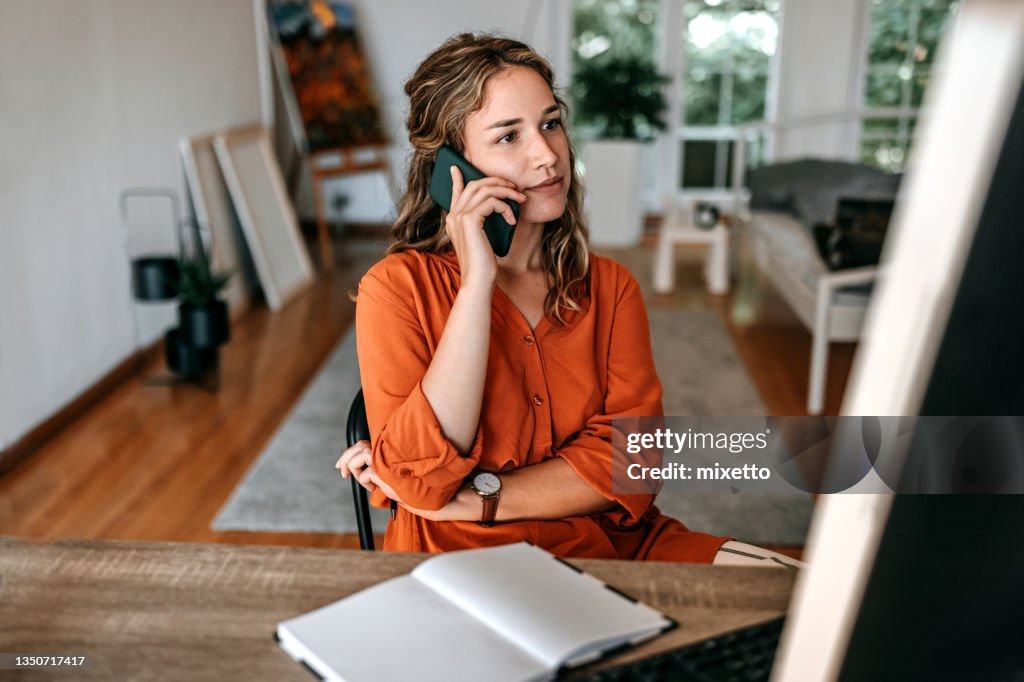 Junge Frau, die im Homeoffice auf dem Smartphone spricht