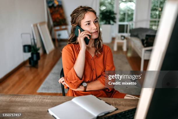 young woman talking on smart phone at home office - ringing stockfoto's en -beelden