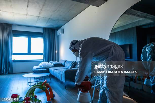 a disinfector in a protective suit and mask sprays disinfectants in the living room - fumigation photos et images de collection