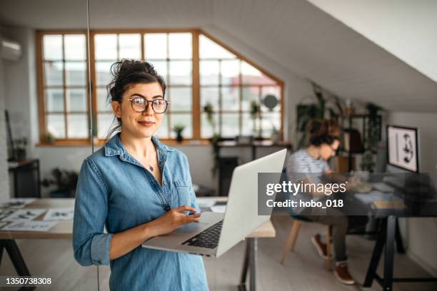 giovane impiegata donna con il computer portatile che guarda la fotocamera - studio di design foto e immagini stock