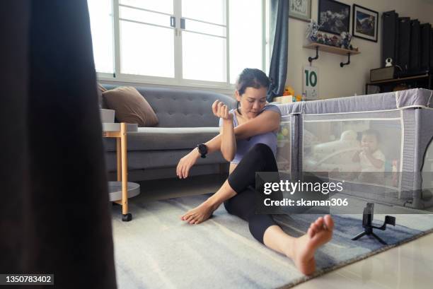 young mother start learning workout and stretching from workout tutorial  video clip from online training course  with daughter playing in playpen - boxen sport stockfoto's en -beelden