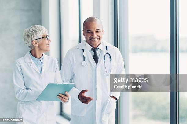 two doctors walking side by side and discussing a medical record - doctors stock pictures, royalty-free photos & images