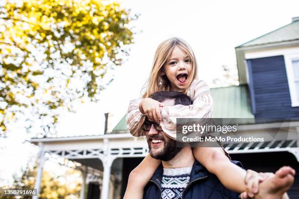 father carrying daughter on shoulders in front of farmhouse - portrait playful caucasian man foto e immagini stock