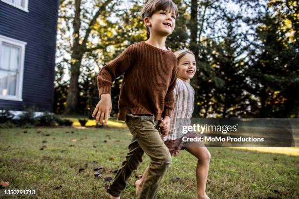 young brother and sister running in front of farmhous - running boy stock-fotos und bilder