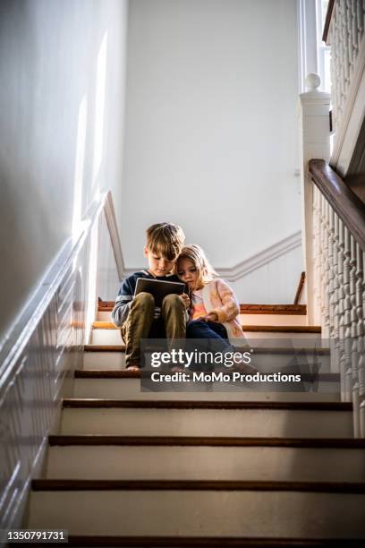 brother and sister watching digital tablet on staircase - step brother stock pictures, royalty-free photos & images