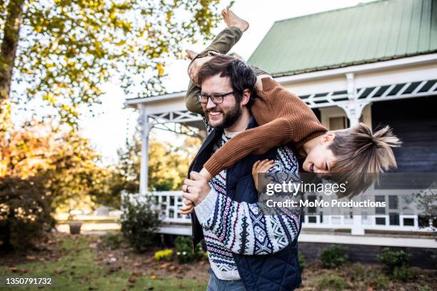 father playing with son in front of farmhouse - wohngebäudeversicherung stock-fotos und bilder