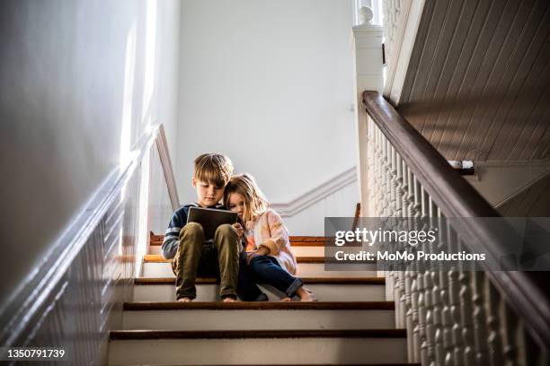 brother and sister watching digital tablet on staircase - sibling stock photos et images de collection