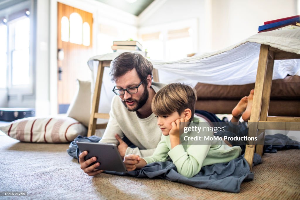 Father and son watching digital tablet in homemade fort