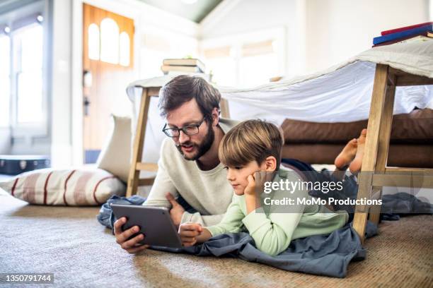 father and son watching digital tablet in homemade fort - internet at home stock pictures, royalty-free photos & images