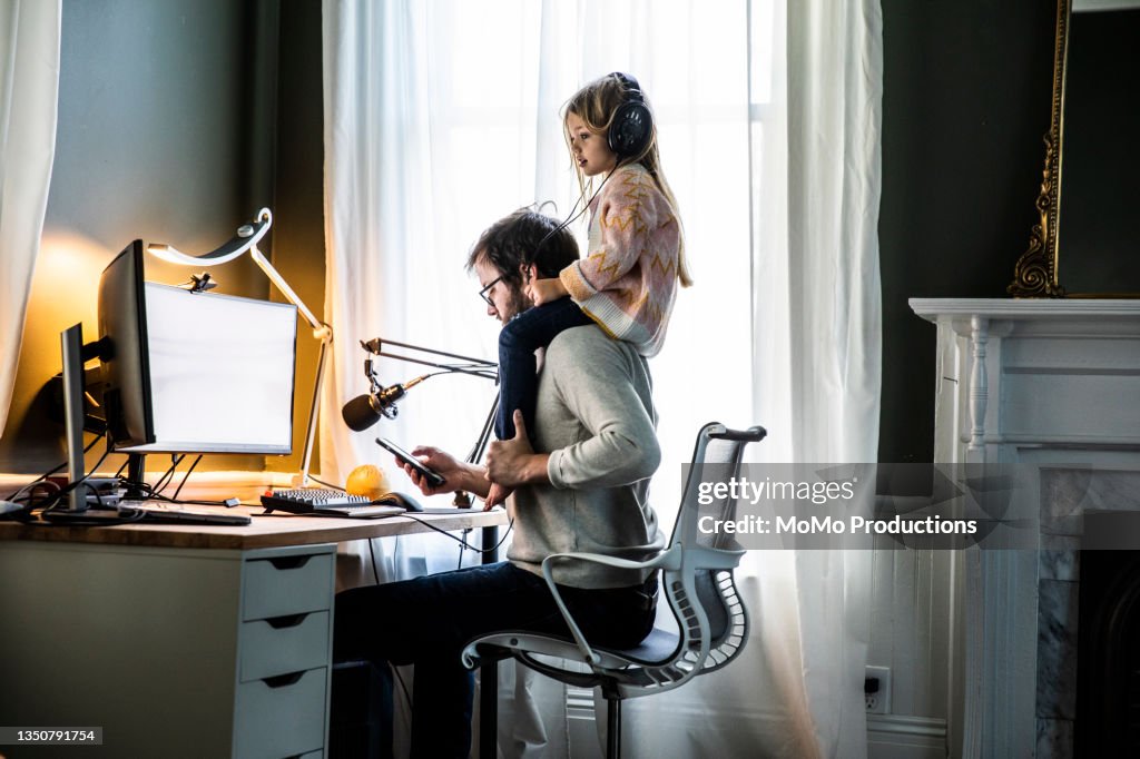 Father working in home office with  young daughter on shoulders