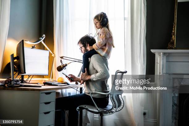 father working in home office with  young daughter on shoulders - working from home stock pictures, royalty-free photos & images