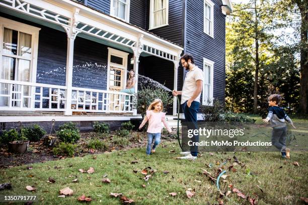 father watering lawn, children playing in hose - two kids playing with hose stock-fotos und bilder