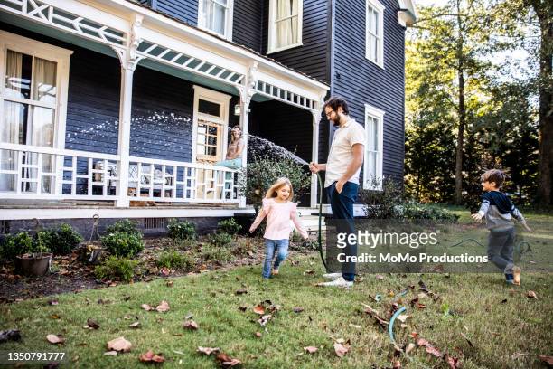 father watering lawn, children playing in hose - two kids playing with hose stock pictures, royalty-free photos & images