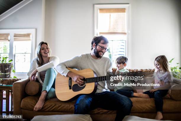 father playing guitar for family in living room - vater sohn musik stock-fotos und bilder