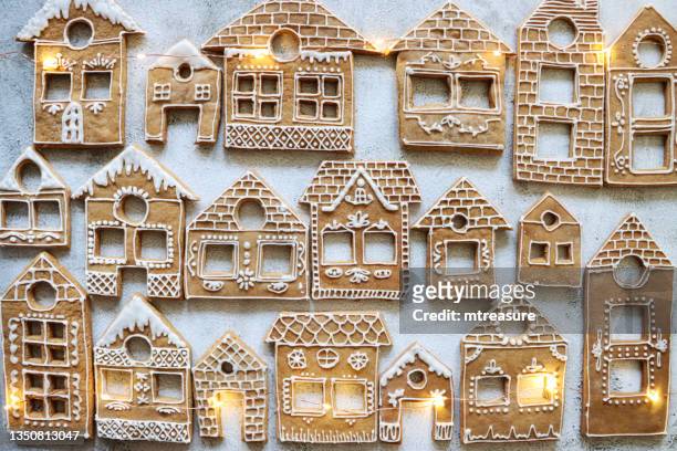 image of rows of homemade, house-shaped, gingerbread biscuits, cookies iced with white glace icing illuminated by fairy lights, christmas village display, marble effect background, elevated view - speculaashuis stockfoto's en -beelden