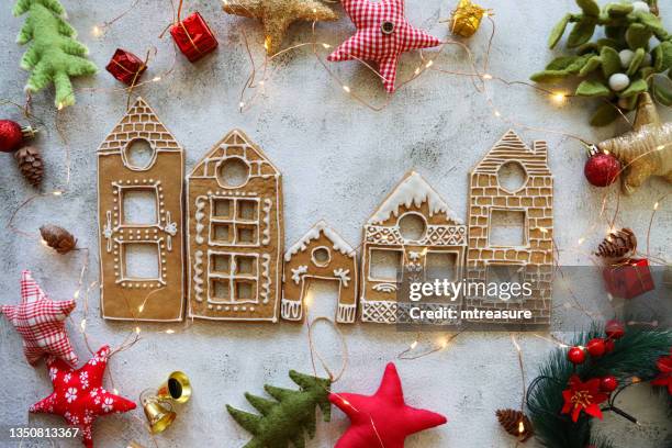 image of row of homemade, house-shaped, gingerbread biscuits, cookies iced with white glace icing, christmas village display surrounded by felt christmas tree and star-shaped ornaments, marble effect background, elevated view - gingerbread biscuit stock pictures, royalty-free photos & images