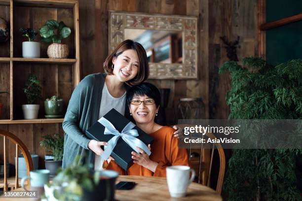 portrait of a senior asian mother receiving a present from her daughter at home. looking at camera with smile. the love between mother and daughter. the joy of giving and receiving - elderly receiving paperwork stock pictures, royalty-free photos & images
