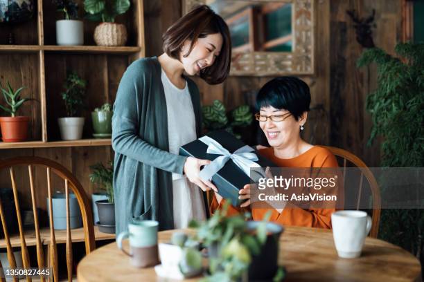 una madre asiática mayor recibiendo un regalo de su hija en casa. el amor entre madre e hija. la alegría de dar y recibir - mother´s day fotografías e imágenes de stock