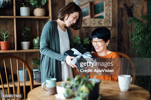 A senior Asian mother receiving a present from her daughter at home. The love between mother and daughter. The joy of giving and receiving A senior Asian mother receiving a present from her daughter at home. The love between mother and daughter. The joy of giving and receiving
