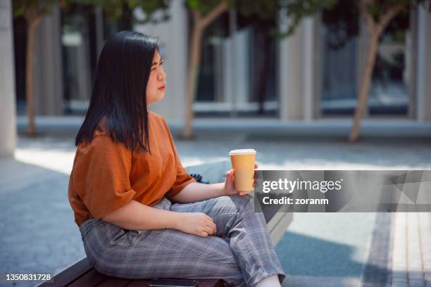 woman holding her reusable cup and sitting on a street bench - cross legged stock pictures, royalty-free photos & images