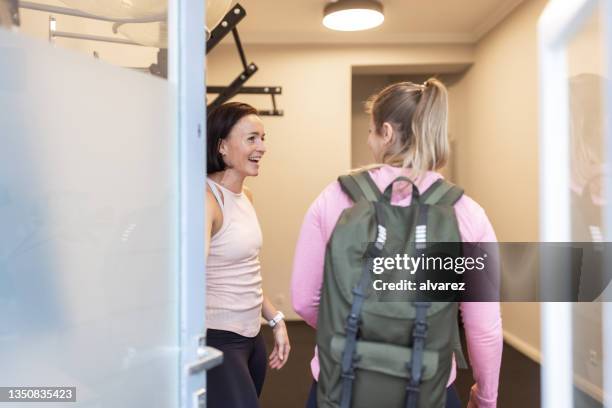 fitness instructor opening the door and welcoming a woman at a gym - open workouts stock pictures, royalty-free photos & images