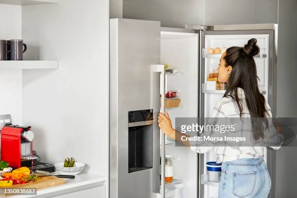 woman looking for food in refrigerator at home - refrigerator stock pictures, royalty-free photos & images