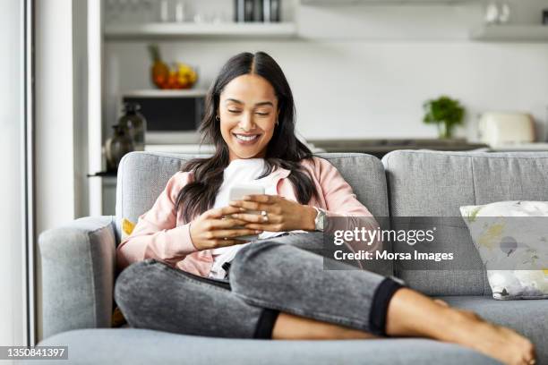 happy woman text messaging on smart phone at home - female sitting on sofa stock pictures, royalty-free photos & images