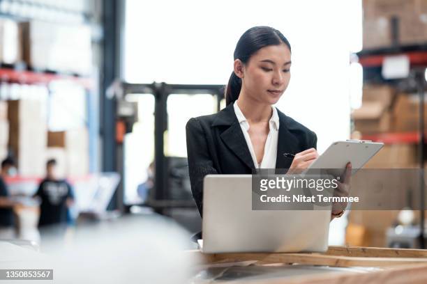 audit process inventory control. asian female warehouse supervisor working on a laptop and checklist to review stock balance inventory in the modern distribution warehouse. - arranging products stock pictures, royalty-free photos & images