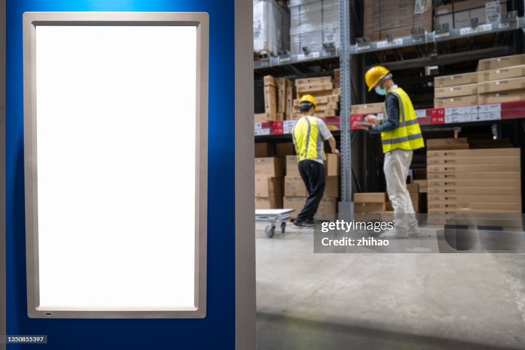 Workers are loading and unloading goods behind the electronic advertising screen