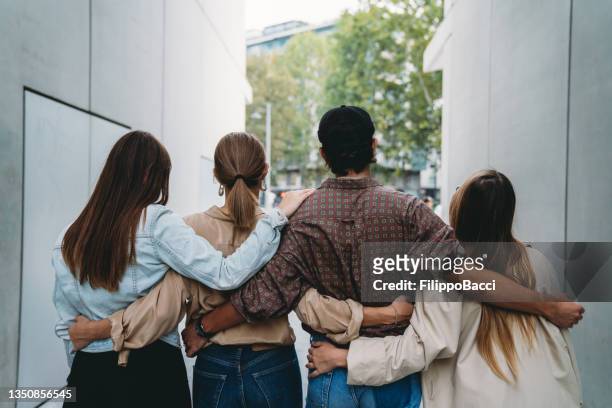 rear view of four friends embracing together - arm in arm stock pictures, royalty-free photos & images