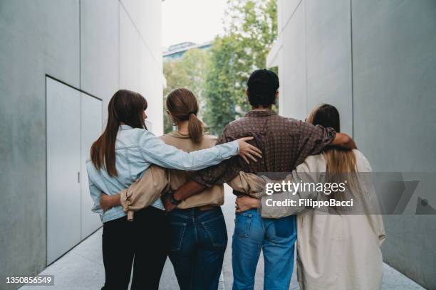 rear view of four friends embracing together - community arm in arm stock pictures, royalty-free photos & images