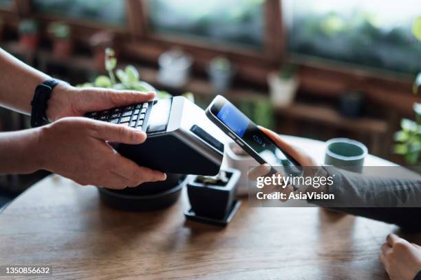 close up of a woman's hand paying bill with credit card contactless payment on smartphone in a cafe, scanning on a card machine. electronic payment. banking and technology - fintech stock pictures, royalty-free photos & images