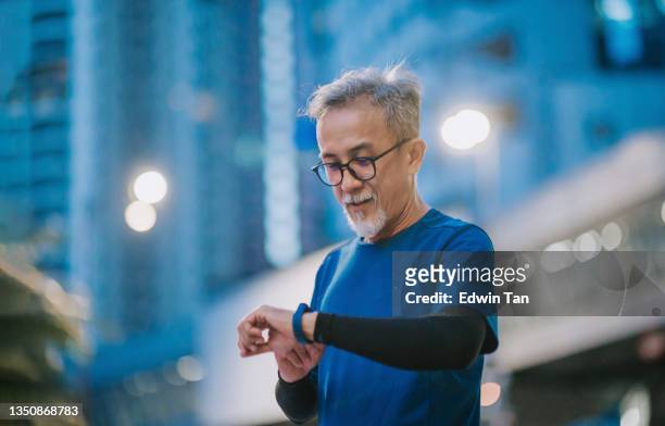 asian chinese senior man checking his heartbeat with fitness tracker after running in the city during late evening - checking sports stock pictures, royalty-free photos & images