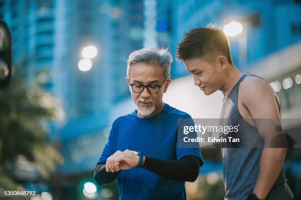 asian chinese senior man and his son checking his heartbeat with fitness tracker after running in the city during late evening - malaysia father and son stockfoto's en -beelden