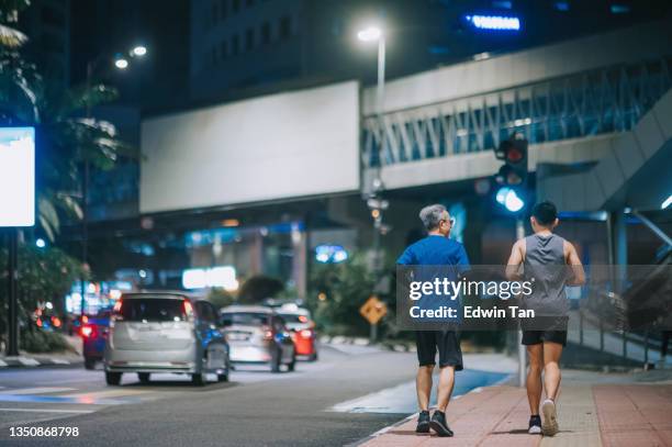 rear view asian chinese active senior man and his son running jogging in the city at night after work together - billboards side by side stock pictures, royalty-free photos & images