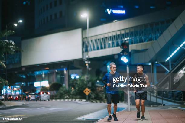 asian chinese active senior man and his son running jogging in the city at night after work together - billboards side by side stock pictures, royalty-free photos & images