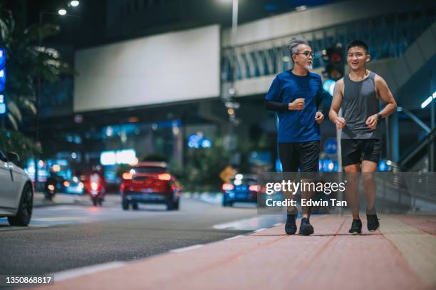 asian chinese active senior man and his son running jogging in the city at night after work together - billboards side by side stock pictures, royalty-free photos & images