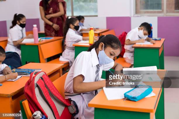students in classroom wearing protective face mask after school reopening - social distancing classroom stockfoto's en -beelden