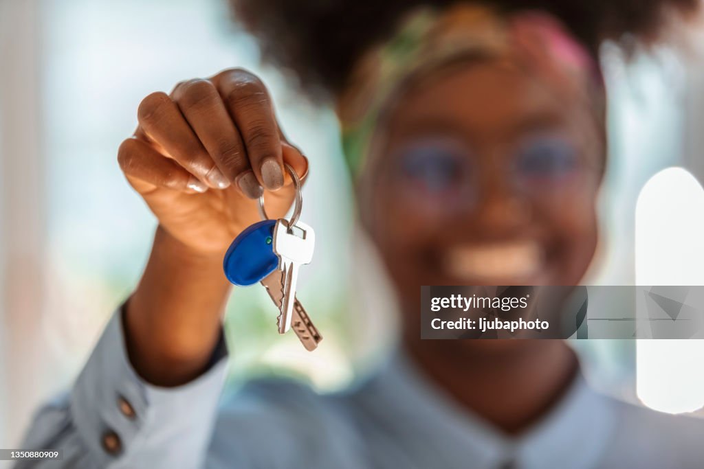 Junge aufrichtige Afroamerikanerin, die Schlüssel zur Kamera zeigt