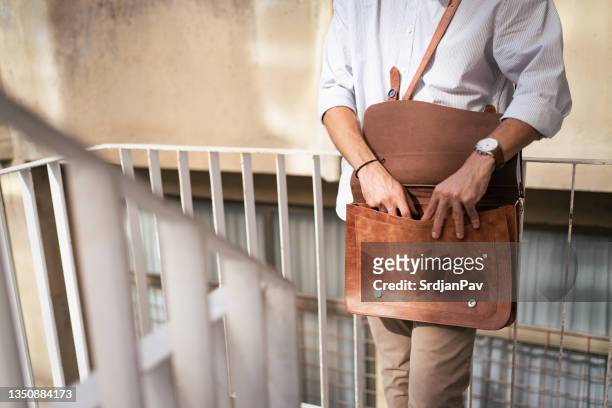 unrecognizable modern male entrepreneur looking for something in his messenger bag - leather bag stock pictures, royalty-free photos & images