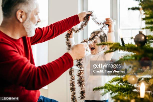 young girl having fun with tinsel while decorating christmas tree - tinsel stock-fotos und bilder