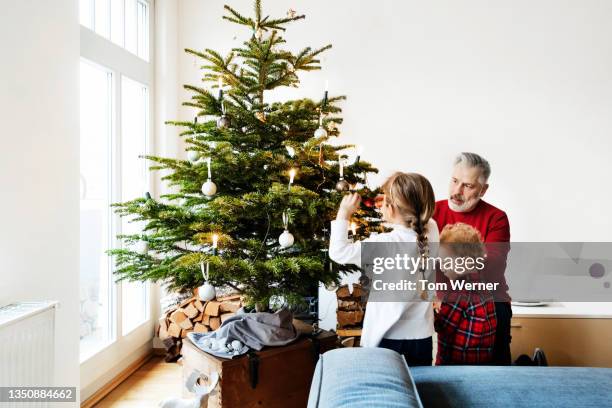 grandpa spending time with grandchildren decorating christmas tree - kerstboom versieren stockfoto's en -beelden