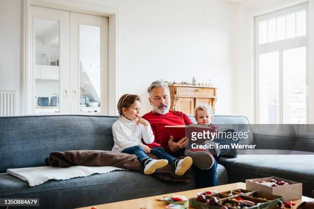 two young grandchildren sitting with grandpa reading book - petit fils photos et images de collection