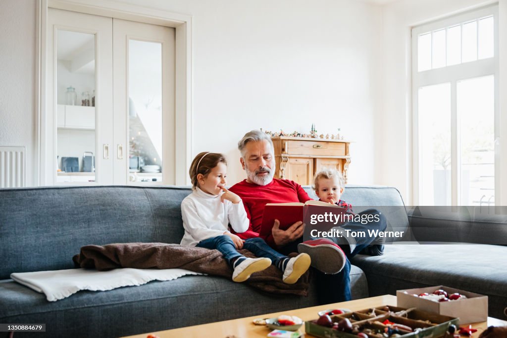 Two Young Grandchildren Sitting With Grandpa Reading Book