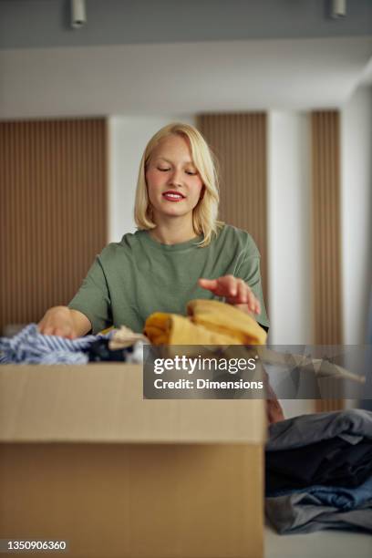 woman folding and packing used clothes into cardboard donation box. - coat check stock pictures, royalty-free photos & images