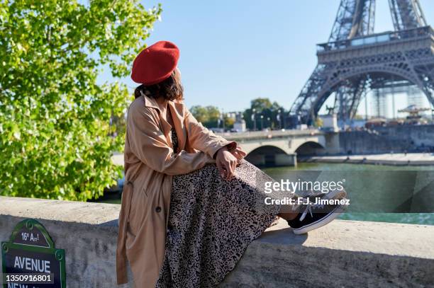 woman sitting relaxed by the eiffel tower, paris - trench coat stock pictures, royalty-free photos & images