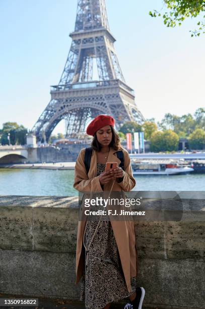 woman using mobile phone with eiffel tower in the background - lange jurk stockfoto's en -beelden