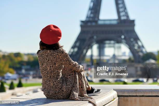 woman sitting in front of the eiffel tower, view from behind - premium paris stock-fotos und bilder