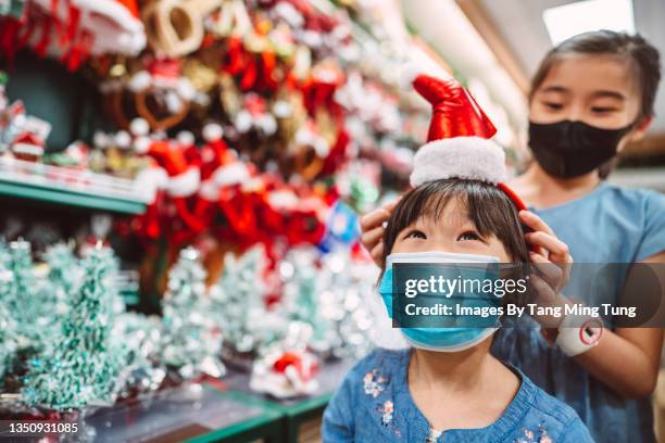 lovely little sisters in protective face masks shopping for christmas accessories in a gift shop joyfully - christmas celebrations in china imagens e fotografias de stock